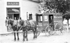 Jake Bentz leans agains the wall and Earl Fischer looks out from the doorway of the Bank building which is now Bernie's Bar, while Iver C. Noste sits in his Watkins wagon in front.